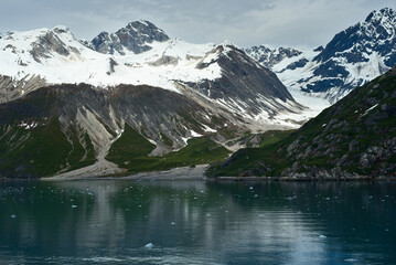 Fototapeta premium Rugged, snowy peaks tower over calm waters dotted with ice in Glacier Bay National Park, Alaska