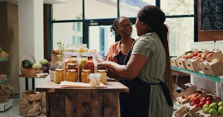 African american vendor giving food sample to shopper, recommending homemade snacks with organic ingredients. Vegan client trying out grocery store products before buying. Handheld shot.