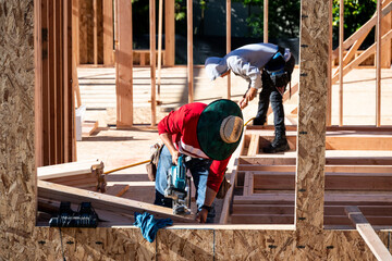 Construction work crew building a new house in a residential neighborhood, wood framing started, sunny summer construction season
