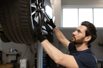 Mechanic focused on repairing car in auto repair shop. Wearing gloves, using tools in professional setting with modern equipment. Dedicated to vehicle maintenance and ensuring customer satisfaction.