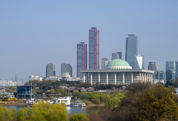 Yeouido, Yeongdeungpo-gu, Seoul, South Korea - March 30, 2023: Spring view of trees at Yanghwa Hangang Park with Seoul Marina near Han River against National Assembly and high rise buildings
