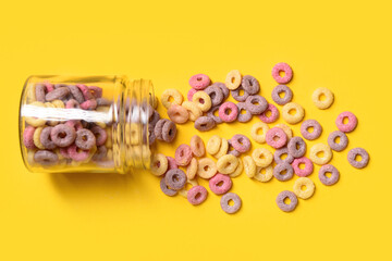 Jar with colorful sweet cereal rings on yellow background