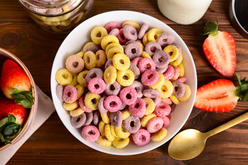 Bowl with colorful sweet cereal rings and strawberries on wooden background