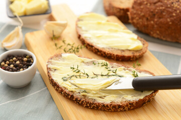 Board of bread slices with fresh butter, garlic and peppercorn on white wooden background