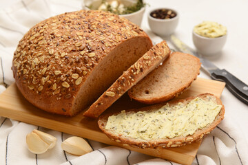 Wooden board of bread slices with fresh butter and garlic on white background