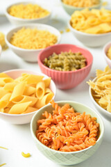 Bowls with different raw tasty pasta on white background, closeup