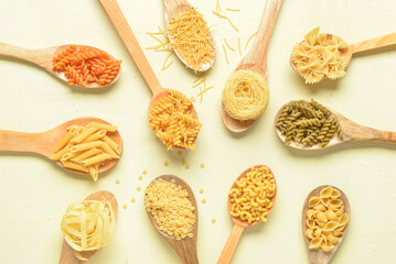Wooden spoons with different raw tasty pasta on light beige background