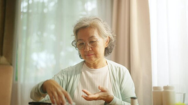 4K Asian senior mature woman patient with diabetes using medical device glucometer checking glucose in blood by herself in bedroom at home. Elderly people self-care and daily health check concept.