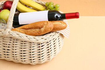 Wicker basket with tasty food and wine for picnic on table against beige background