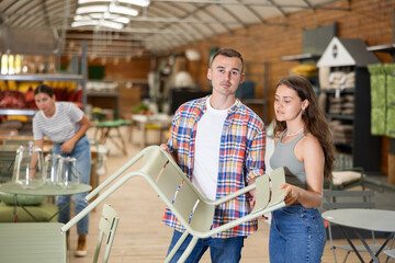 Spouses customer choose chair in garden furniture store showroom center. Young woman and husband runs hand over smooth surface, imagining how it would look in patio