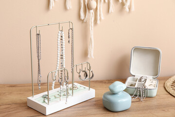 Organizers with stylish different jewelry and perfume bottle on dresser near beige wall