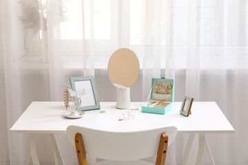 Organizers with stylish different jewelry, mirror and photo frames on table near window