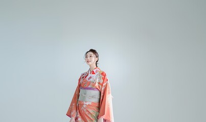 A woman in a traditional Japanese kimono stands in front of a white wall