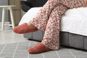 Young woman in red slippers sitting on bed in bedroom, closeup