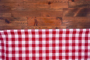 Red and white checkered, plaid tablecloth on wooden surface. Top view. Photograph.