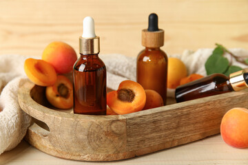 Bottles of cosmetic oil with fresh apricots on wooden background