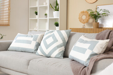 Interior of stylish living room with cozy sofa, pillows, shelving unit and houseplant, closeup