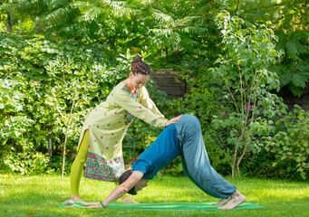 woman teacher helps student perform yoga exercises.woman instructor in sari helps supervise male student doing yoga poses exercises in nature