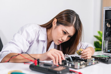 Serious beautiful young woman repairing electronic circuit board or computer parts on her desk. service center, repair service, with gray background.