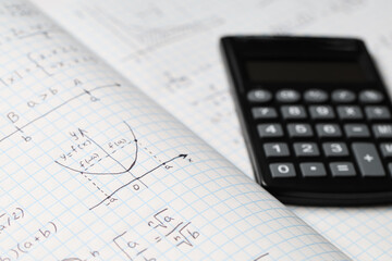 Copybook with handwritten maths formulas and calculator as background, closeup