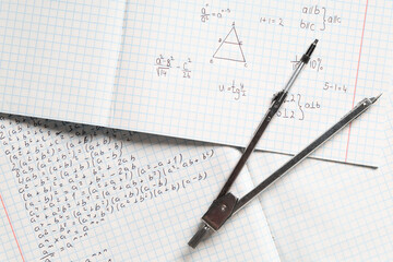 Copybooks with handwritten maths formulas and pair of compasses as background, closeup