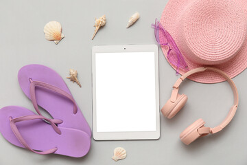 Tablet and beach accessories with flip-flops on grey background. Top view