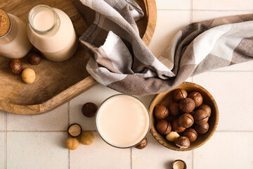 Glass and bottles of fresh macadamia milk on white tile background