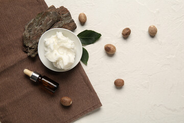 Bowl of shea butter with bottle of cosmetic oil and nuts on white background