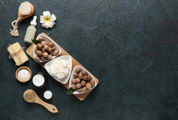 Bowls of shea butter with bottle of cosmetic oil, soap bar and nuts on dark background