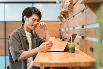 スマホを見てショックを受ける若いアジア人男性（炎上・失敗・ミス・困る・悩む・後悔・自己嫌悪）
