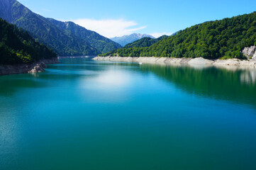 Obraz premium Beautiful Kurobe Dam Reservoir with Blue Sky and Mountains（日本の大きなダム「黒部ダム」の大きな貯水池のきれいな水面と青空と山）