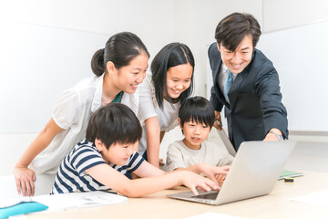 学校の授業でパソコンを使って勉強する小学生の子供達と先生（ICT教育・学校・塾・クラスメイト）
