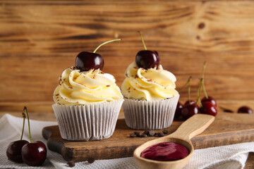 Board with sweet cherry cupcakes and spoon of jam on wooden background