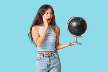 Fototapeta premium Surprised young Asian woman with globe on blue background. Travel concept