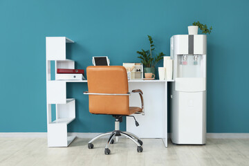 Modern workplace with paper cups and water cooler near blue wall in office