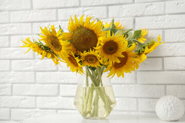 Vase with sunflowers on chest of drawers near white brick wall in room