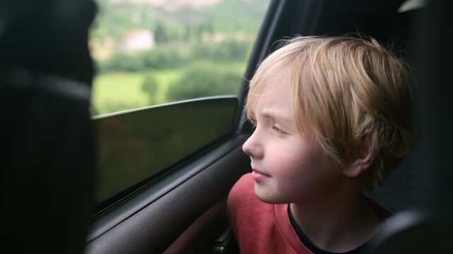 Preteen boy look out through window of car during family road trip and enjoy of pleasant expectation of happy vacation. Glad child travel with parents while holidays. Journey through the countryside