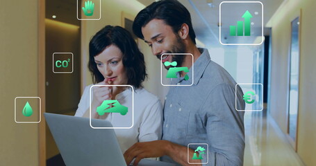 Image of ecology icons over diverse colleagues using laptop in office