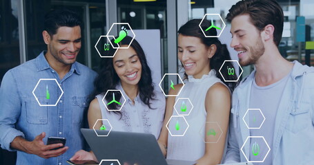 Image of ecology icons over diverse colleagues using laptop in office