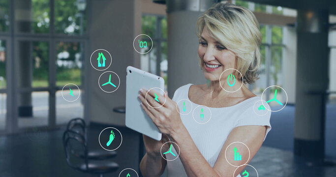 Image of ecology icons over caucasian businesswoman using tablet in office