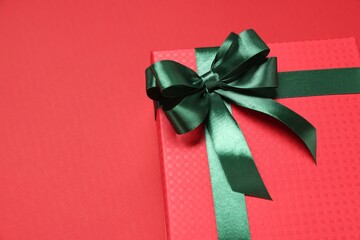 Gift box with green bow on red background, closeup. Space for text