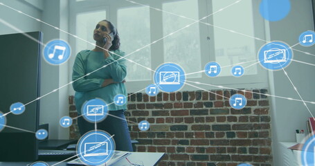 Image of network of connections with icons over biracial businesswoman talking on smartphone