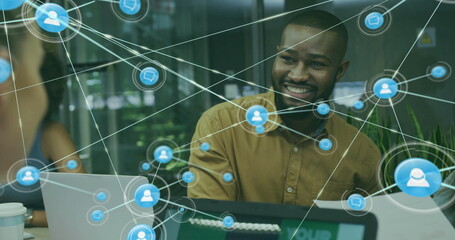 Image of network of connections with icons over diverse colleagues using laptop in office