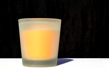 Orange wax candle in a translucent glass with a black background