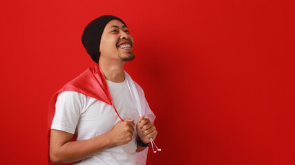 Happy and excited Indonesian man holds Indonesia's flag to celebrate Indonesia Independence Day....