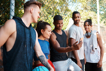 You guys have got to see this. Shot of a group of sporty young people looking at something on a cellphone while standing along a fence outdoors.