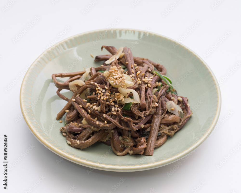 Sticker Close up of seasoned bracken with sesame seeds and onion on ceramic dish and white floor, South Korea
