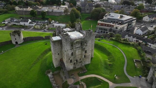 Trim Castle, County Meath, Ireland, October 2023. Drone clockwise orbit pull back of the stone Stronghold ascending to reveal the surrounding Curtain Walls and nearby town with busy roads.