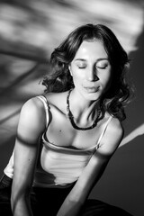 Front portrait of a young woman with long wavy hair, dressed in a white t-shirt and jeans, posing in the shadows and the sunset light.