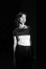 Dramatic portrait of a young woman with long wavy hair, dressed in a white t-shirt and jeans, posing in the shadows and the sunset light.